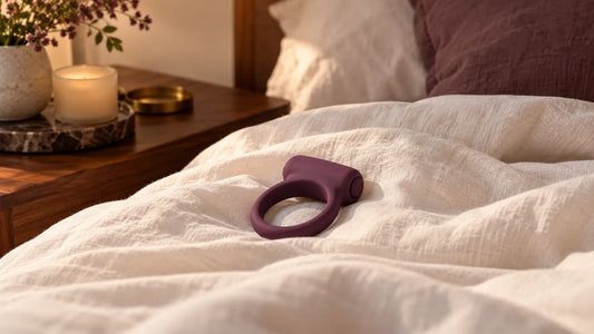 A plum-colored flexible vibrating ring resting on cream bedside linen